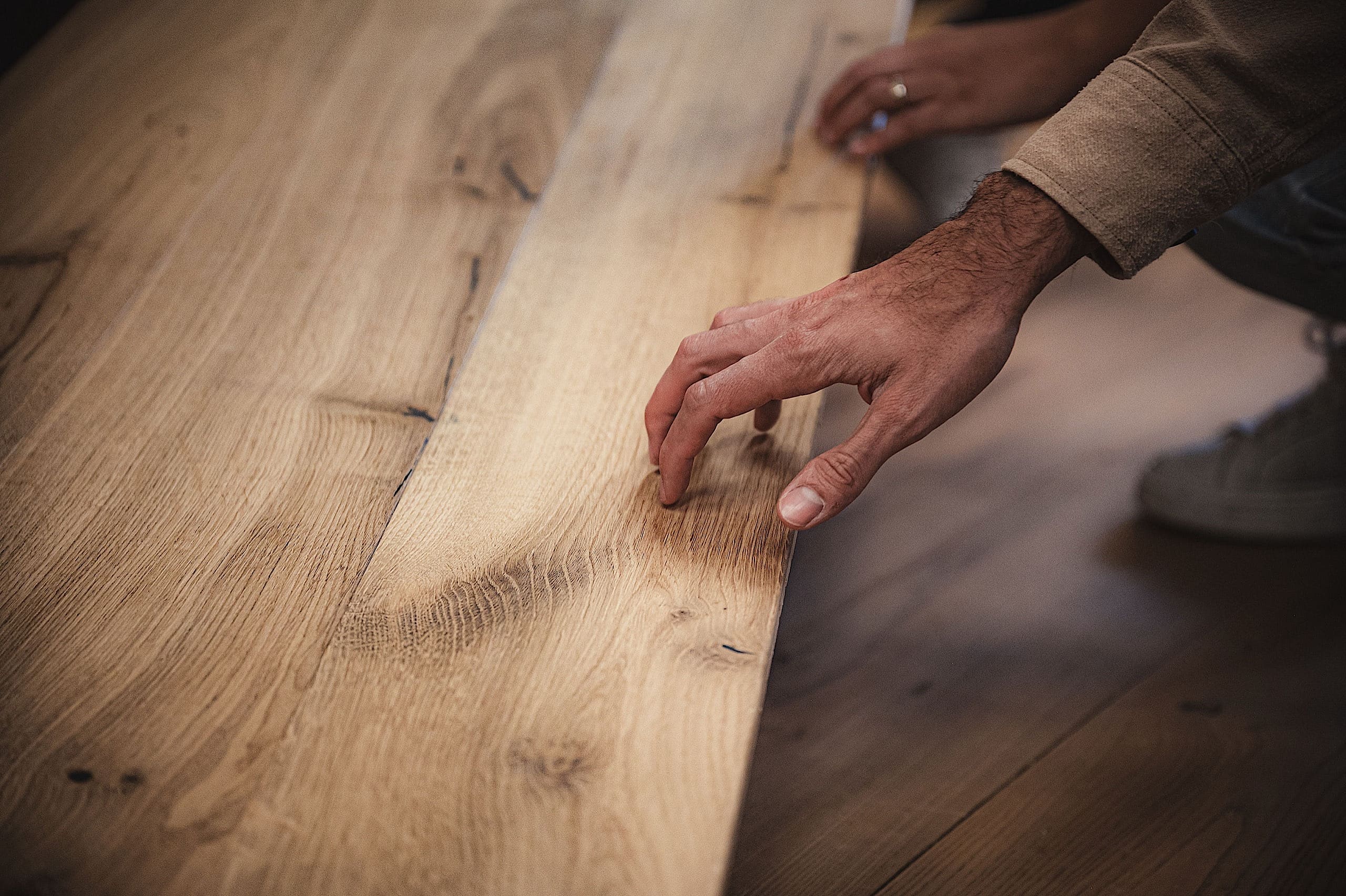 Eine Person verlegt oder prüft Holzdielen, indem sie eine Diele neben der anderen auf einem Holzboden positioniert.