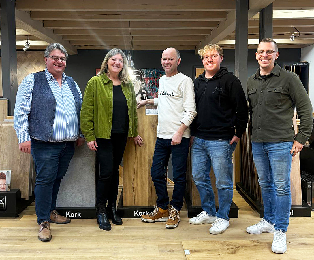 Fünf Personen stehen drinnen auf einem Holzboden und posieren für ein Gruppenfoto vor Schautafeln mit der Aufschrift Kork.
