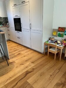 Eine moderne Küche mit weißen Schränken und Holzboden, daneben ein kleiner Kindertisch aus Holz mit Malutensilien.