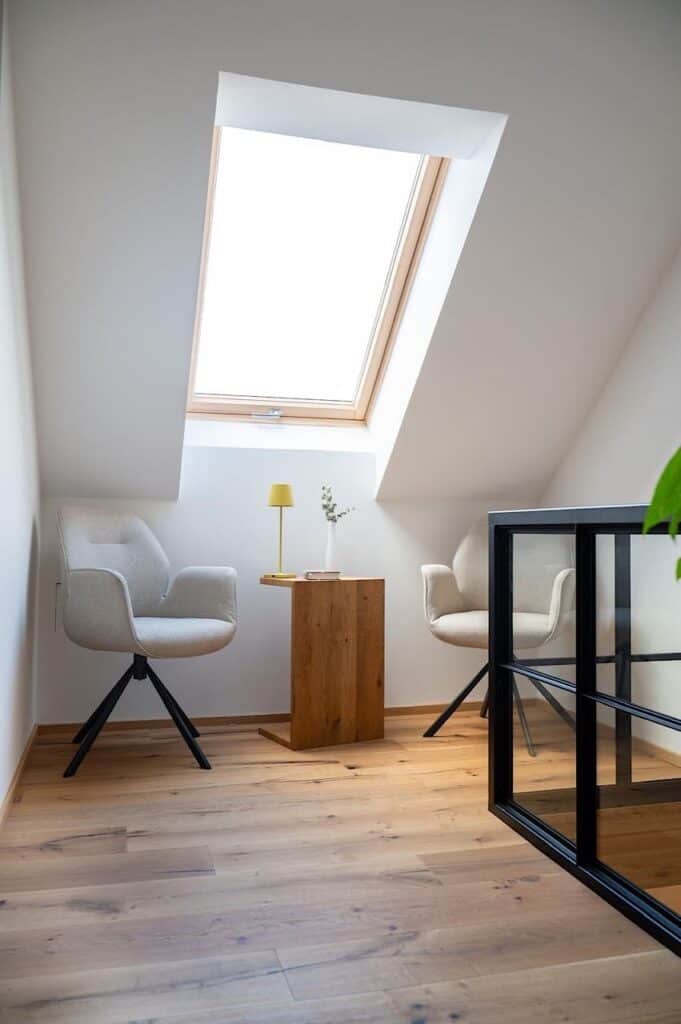 Zwei Stühle und ein kleiner Holztisch, die unter einem schrägen Oberlicht stehen.