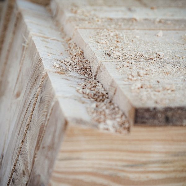 Nahaufnahme von aufeinander gestapelten, grob geschnittenen Holzbrettern, die Sägespuren, Rillen und Holzspäne auf der Oberfläche zeigen.