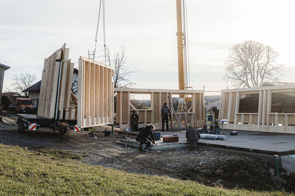 An einem klaren Tag setzen Arbeiter mit einem Kran auf einer Baustelle für ein neues Gebäude hölzerne Wandrahmen zusammen.