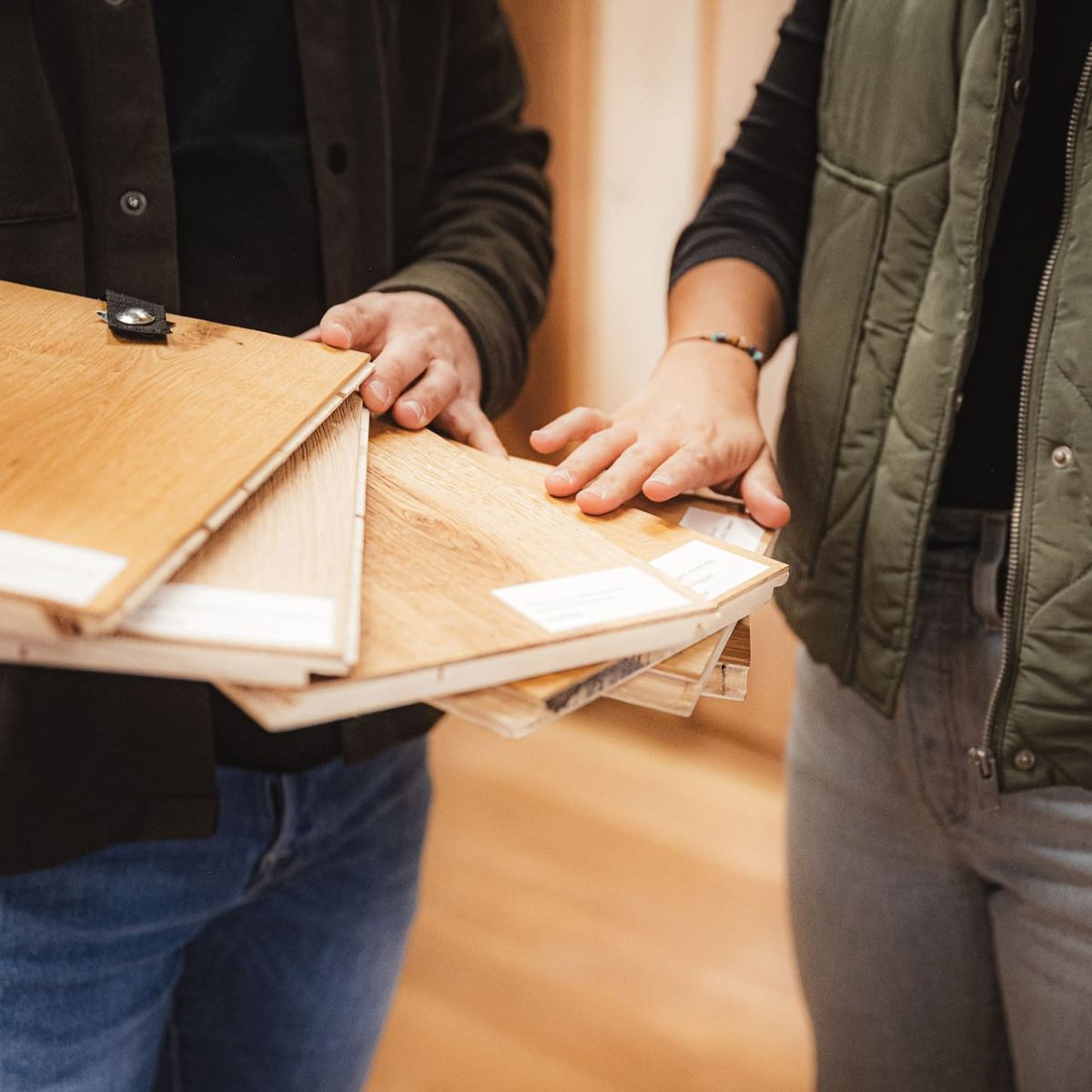 Zwei Personen vergleichen und besprechen mehrere Muster von Holzfußböden, wobei eine Person die Muster in der Hand hält und die andere auf sie zeigt.