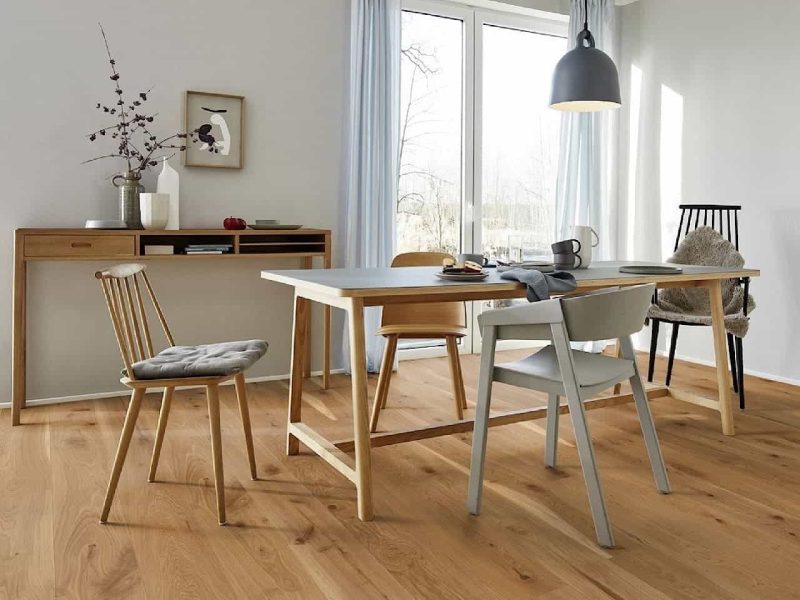 Esszimmer mit einem Tisch aus hellem Holz, verschiedenen Stühlen und einem Konsolentisch an der Wand.