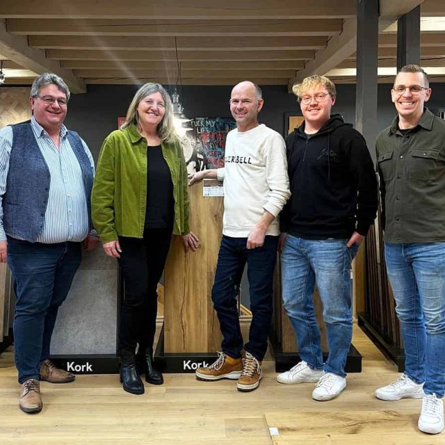 Fünf Personen stehen drinnen auf einem Holzboden und posieren für ein Gruppenfoto vor Schautafeln mit der Aufschrift Kork.